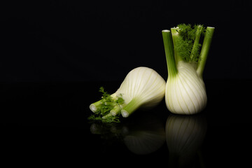 Two fennel vegetables on a black background with reflection