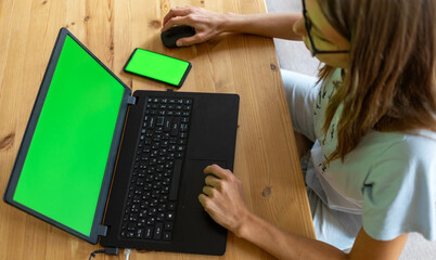 Top view young girl working or studying using her laptop and smartphone with mock up green screens.