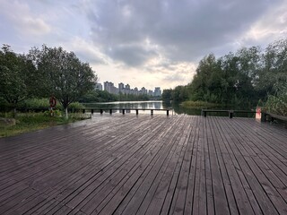 A wooden platform in Yanghu Wetland Park, Hunan, Changsha, China. Trees, lake, building.