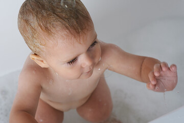 Baby, child and play with bubbles in bath of water for morning routine, skincare and wellness at home from above. Boy, kid and cleaning in tub with soap, foam and bathroom for fun, hygiene or washing