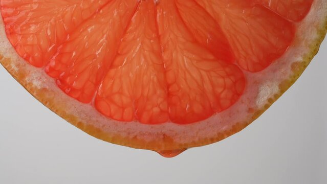 Slice of red grapefruit with juice drops on a white background, macro photography. Texture fresh citrus fruit, close up