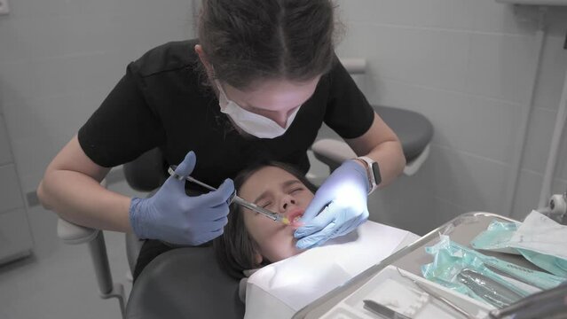 A child winces in pain during an injection of anesthesia into the gum before removing a baby tooth at a pediatric dentist's appointment. Infiltration anesthesia of the teeth of the lower jaw.