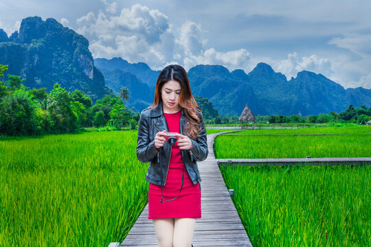 Asian woman walking on a wooden walkway with green rice fields in Vang Vieng, Laos.