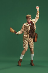 Full-length image of young guy in retro clothes in image of boy scout dancing, having fun against green studio background. Concept of imagination, retro style, fashion, youth, creativity - obrazy, fototapety, plakaty