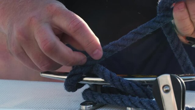 Man sailor shows how ta make figure of eight knot on cleat. Yachtsman fixes mooring rope on cleat on yacht after sailing