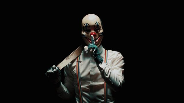 Scary clown holding a knife and asking for silence against black background