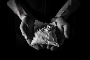 Packet with white narcotic in hand on black background, monochrome  - obrazy, fototapety, plakaty