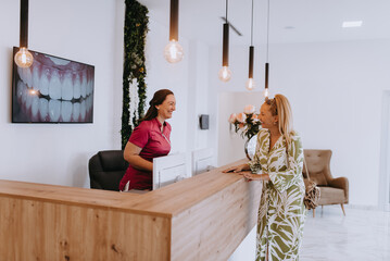A beautiful blonde woman conversing with the dental clinic receptionist, scheduling an appointment...