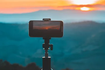 Fototapeten A smartphone is recording the sun setting over a mountain range. © Thananchanok
