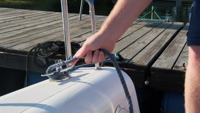 Man sailor expertly undoes mooring ropes from dock cleat. Man initiates sequence to set sailboat in motion for maritime journey