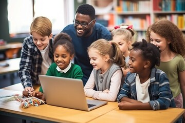Group of children with male teacher using laptop together in modern school classroom.