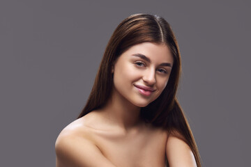 Obraz na płótnie Canvas Young brunette woman with perfect, clean and smooth skin looking at camera against grey studio background. Concept of foundation makeup advertising to highlight matching skin tones, seamless coverage.