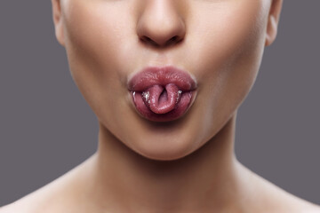 Cropped photo of. Close-up of woman's mouth with twisted tongue, highlighted by subtle lip gloss,...