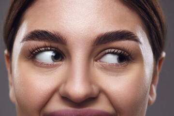 Cropped photo. Close-up of woman's eyes with well-groomed eyebrows, clear eyes, and smooth skin against a grey background. Concept of medical, exercises techniques for vision, and focusing for eyes.