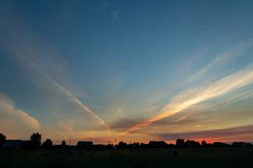 Beautiful evening sky at sunset over silhouettes of houses. Summer landscape.