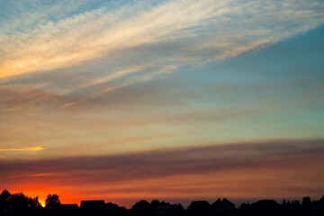 Beautiful evening sky at sunset over silhouettes of houses. Summer landscape.