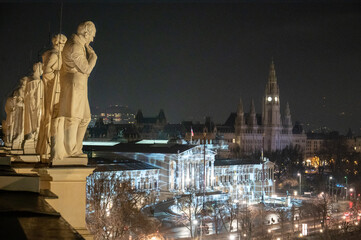 Blick vom Dach mit Statuen auf das nächtlich beleuchtete Parlament in Wien