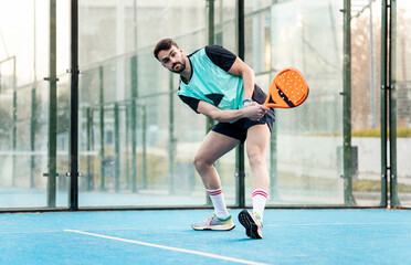 An adult man is playing a game of padel on an outdoor court in sports clothing. The boy has just...