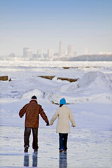 A couple walks across a frozen Lake Erie with the Cleveland skyline in the background.