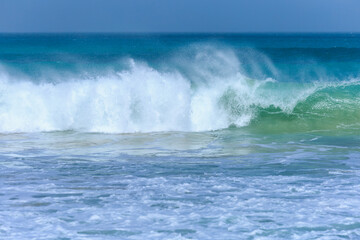 A large wave with turquoise water and white foam approaches on a windy day at Boa Vista's beach, Cape Verde.
