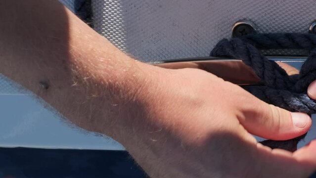 Yachtsman adeptly untangles knot securing mooring ropes to cleat. Man prepares sailboat for imminent departure from harbor