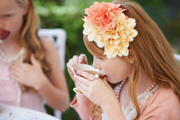 Girl, child and drinking tea in garden with party for birthday, celebration and playing outdoor in home. Person, kid and porcelain cup in backyard of house with dress up, flower and role play fun