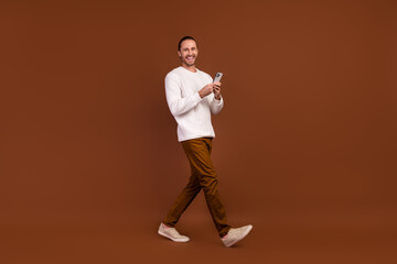 Fototapeta na wymiar Full length photo of cheerful funky guy dressed white pullover communicating modern device isolated brown color background