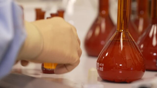 Las manos de una mujer qu&iacute;mica manipulando en el laboratorio con vasos y matraces.