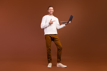 Fototapeta na wymiar Full length photo of positive cheerful guy dressed white pullover showing finger modern device isolated brown color background