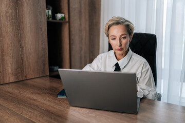 Attractive thoughtful concerned middle-aged adult 50s woman working on laptop computer in office looking to screen, thinking solving problem. Serious pensive businesswoman search inspiration.