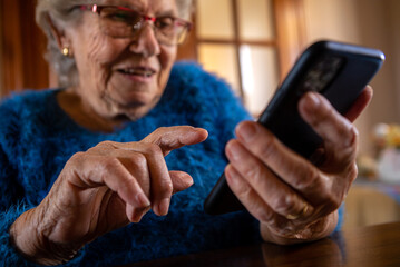 Elderly woman looking at camera while using mobile phone. Happy smiling grandma