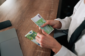 Top view of woman sitting at table, holding euro bills in hands, counting money. Closeup cropped...