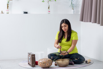 Woman playing a Tibetan bowl inside a white room after meditating