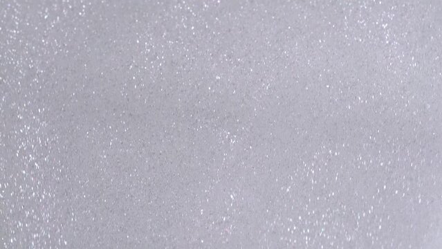 Silver glitter cosmetic product flow down on white background. Liquid drops of lotion with shimmer pouring flow down on canvas. Shiny silver shimmer paint dripping on the white wall