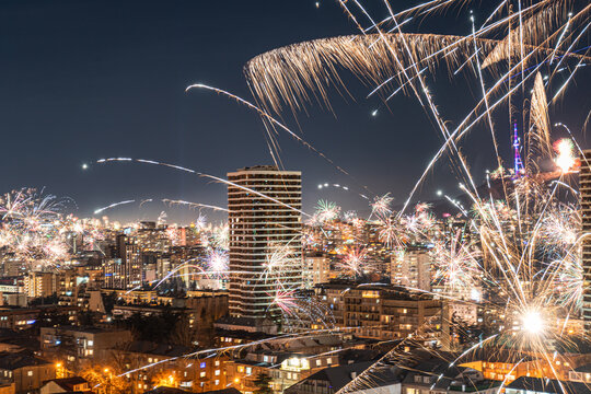 The night sky over Tbilisi bursts with intense fireworks, casting a glow over the cityscape below