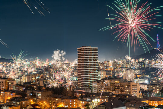 The night sky over Tbilisi bursts with intense fireworks, casting a glow over the cityscape below