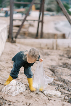 Little girl collects garbage on a sandy beach in a bag, bending over