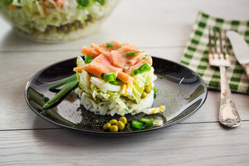 Layered salad of cabbage and other vegetables with pieces of red fish in a plate.
