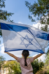 Girl Proudly Holding An Israeli Flag Up High, Back Turned, Outdoors.