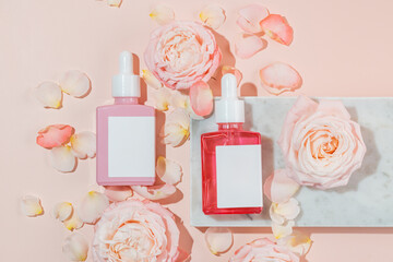 Glass dropper bottles with serum on a marble podium on a pink background with tender pink roses and...