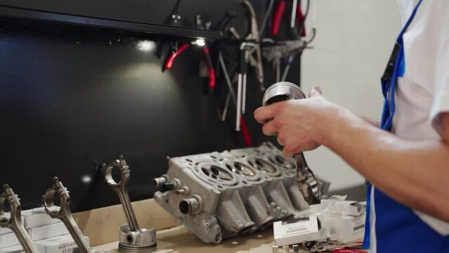 Professional mechanic assembles engine kit, installs piston rings, prepares cylinder block in workshop. Skilled technician at engine rebuild, auto repair tutorial, DIY service guide.