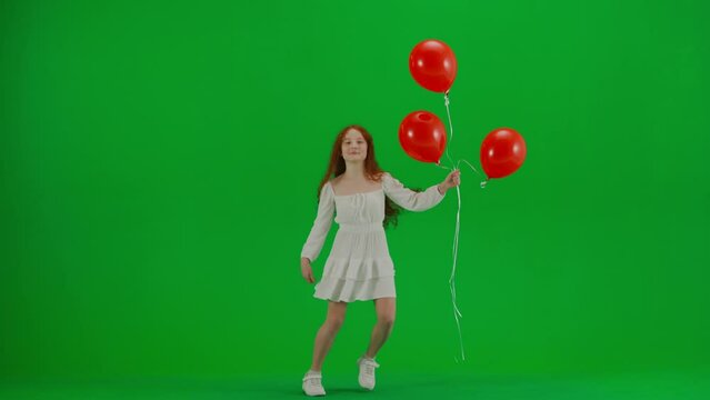 Little girl in white dress with red helium balloons on chroma key green screen isolated background dancing smiling, happy face expression.