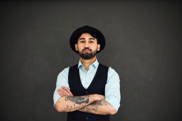 Studio portrait of handsome ethnic male with crossed tattooed arms, dressed in a blue shirt