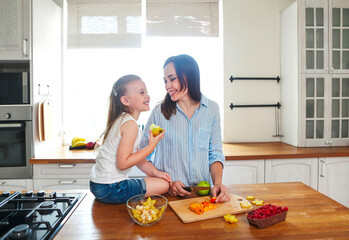 Beautiful little girl with her mother in the kitchen preparing a fresh fruit salad