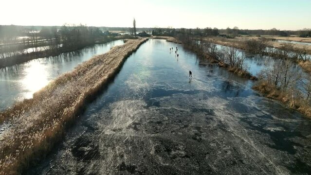 Ice skating on a frozen lake in the Weerribben Wieden nature reserve seen from above during a cold winter day in The Netherlands.