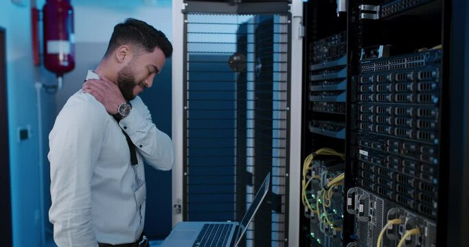 Man, working and neck pain from injury or burnout from stress in server room with technician. IT, programmer and person tired from fatigue and fixing mistake, error or glitch in datacenter technology