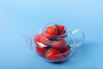 Glass transparent teapot full of red ripe strawberries on a blue background. Summer is a healthy drink. Summer berry tea