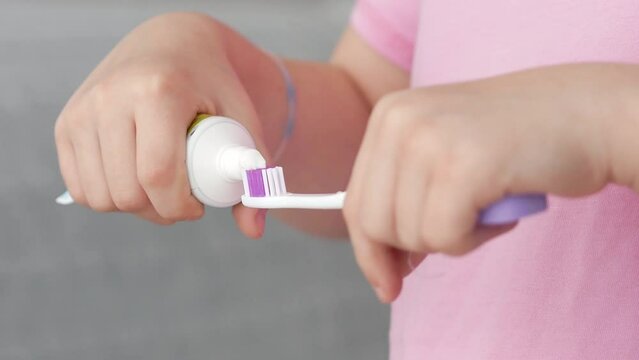 The hands of a girl in a pink sweater squeeze toothpaste onto a toothbrush in the bathroom at home, healthcare, dentistry, oral hygiene. The concept of the morning is the mode of the day.