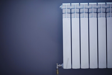 White modern aluminum radiator battery for hot water heating, on the background of a wall in the interior of an apartment or office space.