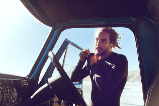 Young male surfer putting on wetsuit after arriving on the beach
